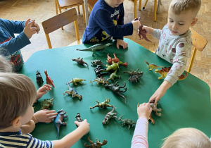 Na zdjęciu dzieci bawiące się dinozaurami przy zielonym stole
