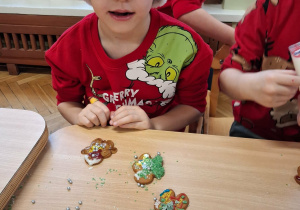 Na zdjeciu chłopiec ubrany na czerwono w mikołajowej czapce, chłopiec ozdabia pierniki