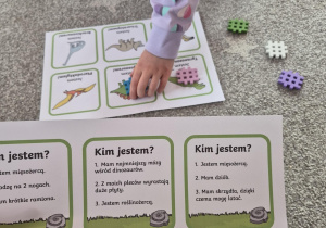 Na zdjęciu gra edukacyjna o dinozaurach jedno z dzieci gra w tą grę, nakładając klocki na karty tematyczne