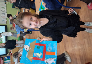 Na zdjeciu dziewczynka prezentująca wykonaną pracę plastyczną karmnik dla ptaków.