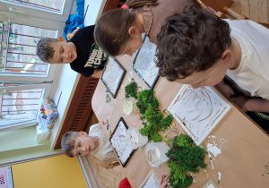Dzieci pracują przy stołach na stole leżą zielone materiały przez dziećmi leżą plastikowe tacki