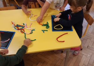 Zdjęcie zabaw przy stoliku w grupie żółtej, dzieci układają kształty z kolorowych drucików.