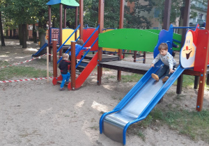 Dzieci z grupy żółtej bawią się w ogrodzie przedszkolnym na zabawce ze zjeżdżalnią.