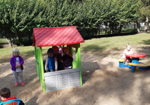 Dzieci z grupy żółtej bawią się w ogrodzie na piasku w kolorowym plastikowym domku