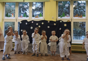 Dzieci recytujące wierszyk podczas przedstawienia choinkowego na tle granatowych dekoracji