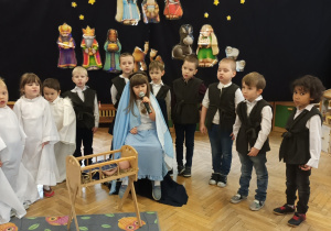 Zdjęcie dzieci z grupy fioletowej podczas przedstawienia choinkowego Dzieci skupione wokół Maryi śpiewają kolędę