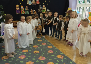 Zdjęcie dzieci z grupy fioletowej, dzieci przebrane za aniołów oraz pasterzy stoją na tle dekoracji.