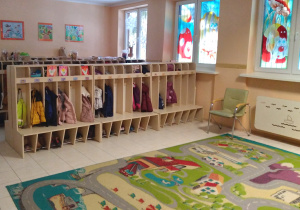 Na zdjęciu duża szatnia w przedszkolu na wprost szafki z ubraniami dzieci, obok dywan