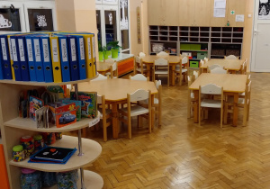 Na zdjęciu grupa pomarańczowa, na fotografii widać stoły i krzesła przy, których na codzień siedzą dzieci oraz półkę z segregatorami i zabawkami