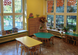 Na zdjęciu sala grupy żółtej na zdjęciu widoczne 2 stoły w kolorach zielonym i żółtym oraz okna przyozdobione dekoracjami