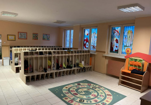 Na zdjęciu szatnia w holu głównym na zdjęciu szafki dzieci obok dywan do zabaw oraz kącik teatralny