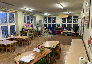 Na zdjęciu grupa zielona, na fotografii po prawej znajduję się tablica multimedialna, na wprost komputer, obok komputera znajduję się kącik plastyczny w kształcie jabłka, na środku klasy znajduję się dywan