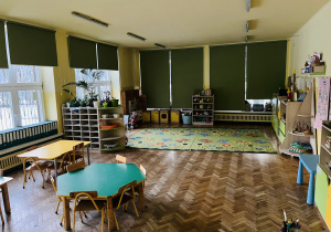 Na zdjęciu sala grupy żółtej na zdjęciu widoczne 2 stoły w kolorach zielonym i żółtym oraz dywan i zabawki