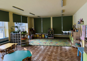 Na zdjęciu sala grupy żółtej na zdjęciu widoczne 2 stoły w kolorach zielonym i żółtym oraz okna przyozdobione dekoracjami